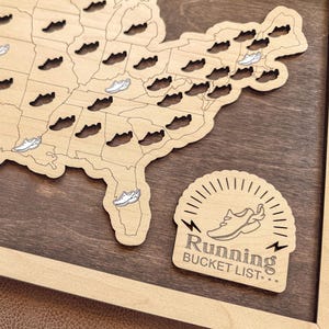May include: Wooden map of the United States with running shoe cutouts. The map is framed and has a dark brown background. A separate sign reads "Running Bucket List..." with a running shoe graphic.