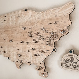 May include: A wooden map of the United States with state abbreviations and pin markers. A separate wooden plaque with the text "HYDER FAMILY PRO SPORTS TOUR" and sports-related graphics is also visible.