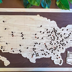 May include: A wooden map of the United States with brown football-shaped markers on each state. The map is framed in light wood and has a brown background. The text "HYDER" and "FBS STADIUM TOUR" is printed below the map.