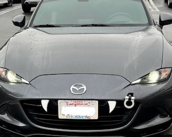 Könnte beinhalten: Ein grauer Mazda Miata mit einem kalifornischen Nummernschild und einem Paar weißen Plastikzähnen, die an der vorderen Stoßstange befestigt sind.