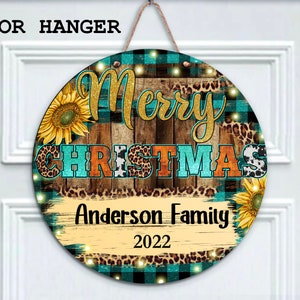 Pu&ograve; includere: Appendiporta rotondo in legno con sfondo a quadri turchese, nero e bianco. Le parole "Merry Christmas" sono in lettere dorate glitter su uno sfondo di assi di legno. Le parole "Anderson Family 2022" sono scritte in nero su uno sfondo di assi di legno. L'appendiporta &egrave; decorato con girasoli, stampa leopardata e stampa di mucca bianca.