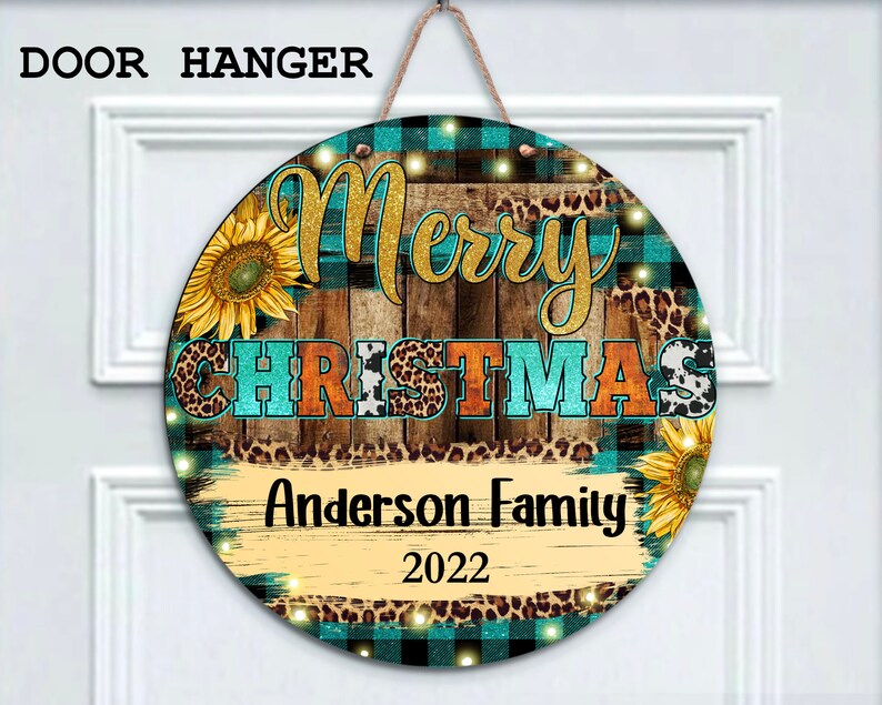 Pu&ograve; includere: Appendiporta rotondo in legno con sfondo a quadri turchese, nero e bianco. Le parole "Merry Christmas" sono in lettere dorate glitter su uno sfondo di assi di legno. Le parole "Anderson Family 2022" sono scritte in nero su uno sfondo di assi di legno. L'appendiporta &egrave; decorato con girasoli, stampa leopardata e stampa di mucca bianca.