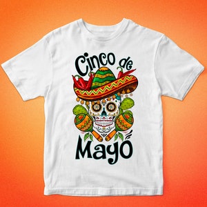 May include: White t-shirt with a colorful graphic design featuring a sugar skull wearing a sombrero, chili peppers, and maracas. The text "Cinco de Mayo" is printed below the skull.