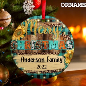 Pu&ograve; includere: Un addobbo natalizio rotondo con uno sfondo in legno rustico, un motivo a quadri blu e neri e un design a stampa leopardata. L'addobbo presenta il testo "Merry Christmas" in lettere dorate glitterate e "Anderson Family 2022" in lettere bianche.