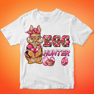May include: White t-shirt featuring a cartoon bunny wearing glasses, a pink bandana, and a pink camo vest. The text "EGG HUNTER" is printed in pink and brown camo lettering, with three decorated Easter eggs below.