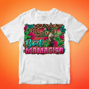 May include: White t-shirt with a graphic of a donkey wearing sunglasses and a bandana. The donkey is surrounded by cacti, flowers, and a leopard print background. The text "Bad Mamacita" is written in pink and turquoise letters.