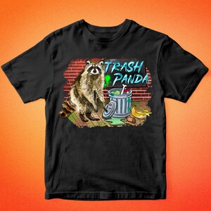 May include: Black t-shirt with a graphic of a raccoon standing next to a trash can with the text "Trash Panda" above it.