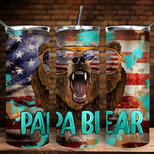 K&ouml;nnte beinhalten: Drei Edelstahlbecher mit patriotischem Thema. Jeder Becher zeigt einen braunen B&auml;ren mit Sonnenbrille und einem rot-wei&szlig;-blauen amerikanischen Flaggenmuster. Der Text "Papa Bear" ist in T&uuml;rkis auf der Vorderseite jedes Bechers aufgedruckt.