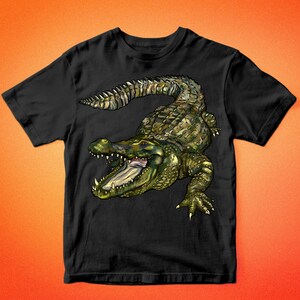 May include: Black t-shirt with a green and brown alligator graphic. The alligator is facing the viewer with its mouth open and teeth showing. The t-shirt has a crew neck and short sleeves.