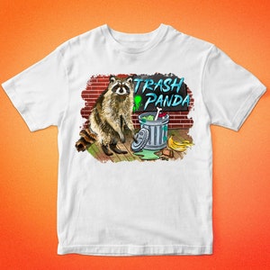 May include: White t-shirt with a graphic of a raccoon standing next to a trash can. The trash can has a sign that says "Trash Panda".