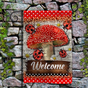 May include: A red and white garden flag with a mushroom and ladybugs. The mushroom has white spots and the flag says "Welcome".