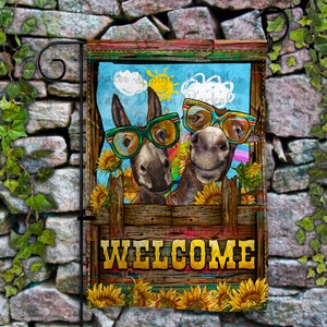 Peut inclure: Un drapeau de jardin de bienvenue avec deux ânes portant des lunettes de soleil et une pancarte en bois qui dit "WELCOME". Les ânes sont entourés de tournesols.