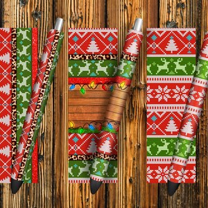 May include: Four different Christmas-themed patterned pens. The pens are red, green, and white with a snowflake, reindeer, and Christmas tree design. The pens are on a wooden background.