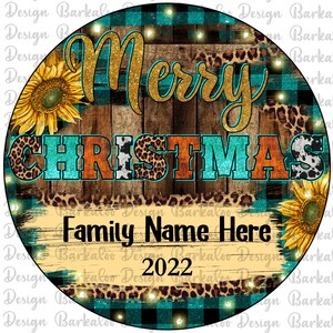 Pu&ograve; includere: Un ornamento natalizio rotondo a quadri blu-verde e nero con uno sfondo in legno. L'ornamento presenta le parole "Buon Natale" in lettere dorate con glitter e un design a girasole. Il testo "Nome della famiglia qui 2022" &egrave; scritto in nero su uno sfondo bianco.