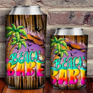 May include: Two colorful can coolers with a wood grain background. The design features palm trees, birds, and the text "Beach Babe".