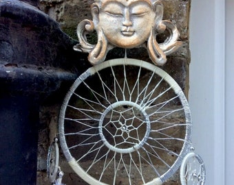 May include: A white and silver dream catcher with white feathers hanging from the bottom. A silver Buddha head is attached to the top of the dream catcher.