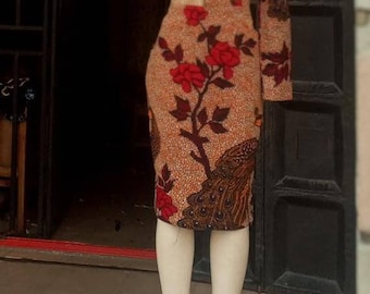 May include: A dress form wearing a brown and red dress with a floral and peacock design. The dress has one long sleeve and one short sleeve.