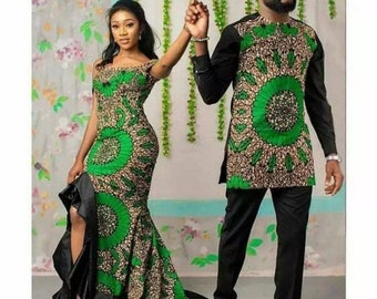 May include: A couple wearing matching green and black patterned outfits. The woman's dress has a black ruffle at the bottom and a slit on the side. The man's shirt has a green and black pattern and is paired with black pants.