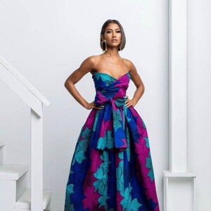 May include: A strapless maxi dress with a floral print in shades of teal, blue, and pink. The dress has a fitted bodice and a flowing skirt. The dress is tied at the waist with a large bow.
