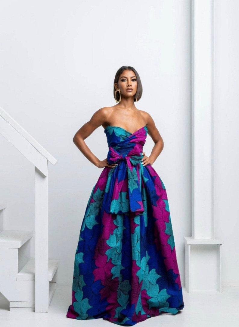 May include: A strapless maxi dress with a floral print in shades of teal, blue, and pink. The dress has a fitted bodice and a flowing skirt. The dress is tied at the waist with a large bow.