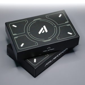 May include: Two black rectangular boxes stacked on top of each other. The top box features a white "A" logo within a gray circular design. The boxes have a futuristic design with the word "RELEASE" and "ALERATION" printed on them.