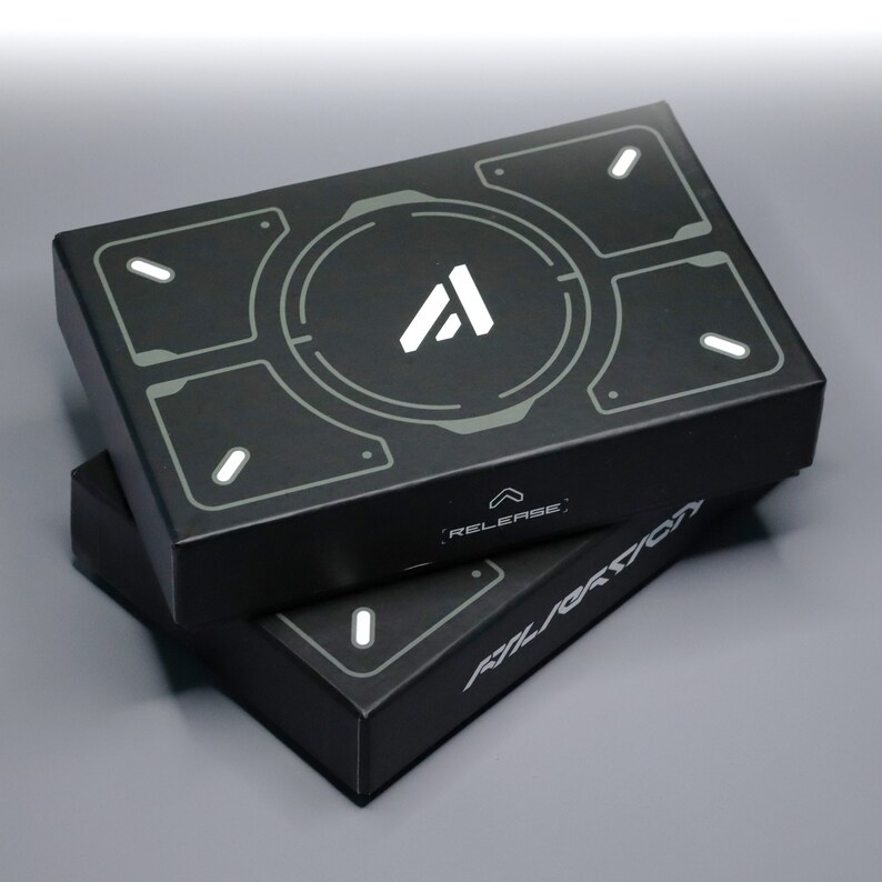 May include: Two black rectangular boxes stacked on top of each other. The top box features a white "A" logo within a gray circular design. The boxes have a futuristic design with the word "RELEASE" and "ALERATION" printed on them.