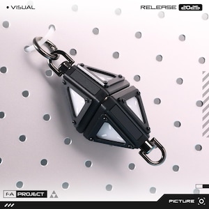 Op de afbeelding: Een zwart en zilver geometrisch sleutelhanger met witte driehoekige lichten. De sleutelhanger is bevestigd aan een zilveren ring en hangt aan een wit pegboard. De tekst "RELEASE 2025" is zichtbaar.