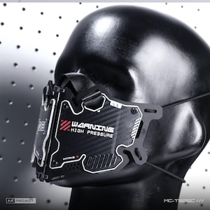 Op de afbeelding: Een zwart gezichtsmasker met een koolstofvezeltextuur en witte en rode tekst met de tekst WARNING HIGH PRESSURE en INTAKE. Het masker heeft een stijf, hoekig ontwerp met zichtbare schroeven, zwarte banden en een doorzichtig plastic accentstuk.