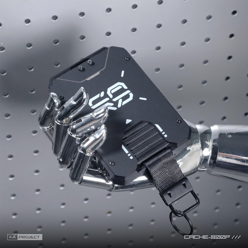 May include: A matte black rectangular wallet with white geometric graphics and the text CACHE-800P. The wallet features a black nylon strap with a metal key ring attachment, secured by visible screws on the front panel surface.
