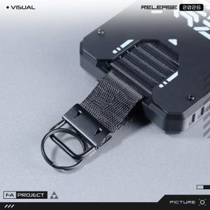 May include: A black rectangular device with a matte finish, featuring white geometric accents and the text "VISUAL" and "RELEASE 2026". It includes a black nylon strap attached to a metal split ring, with "FA PROJECT" printed on the lower left corner.