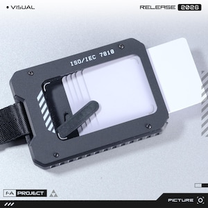 May include: A black metal card holder with a rectangular frame featuring the text ISO/IEC 7810. The device holds multiple white cards and includes a black strap attached to the side. The design has a technical aesthetic with visible screws.