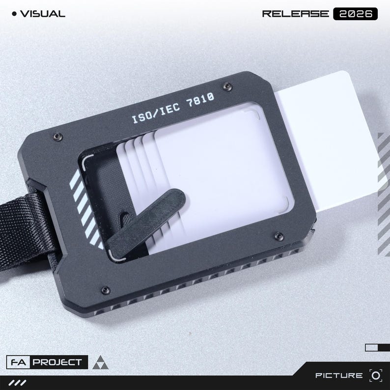May include: A black metal card holder with a rectangular frame featuring the text ISO/IEC 7810. The device holds multiple white cards and includes a black strap attached to the side. The design has a technical aesthetic with visible screws.