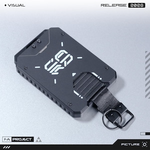 May include: A matte black metal card holder featuring a geometric design with white printed text that reads CRUX. The rectangular accessory includes a black nylon strap with a metal key ring attached to one side and visible screw fasteners.