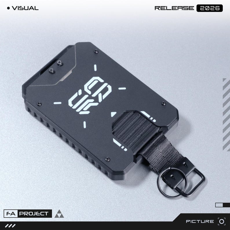 May include: A matte black metal card holder featuring a geometric design with white printed text that reads CRUX. The rectangular accessory includes a black nylon strap with a metal key ring attached to one side and visible screw fasteners.