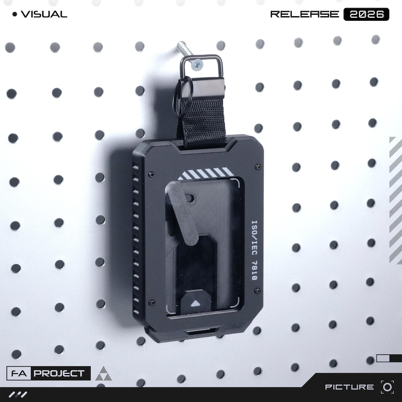 May include: A black rectangular card holder with a rugged frame, featuring a clear window, a black nylon strap with a metal ring, and the text ISO/IEC 7818 printed on the side. The holder is suspended from a metal screw.