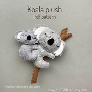 May include: A PDF pattern for sewing a gray felt koala plush toy with a smaller koala on its back. The koalas have white ears and black eyes. The pattern includes sewing instructions and a video.
