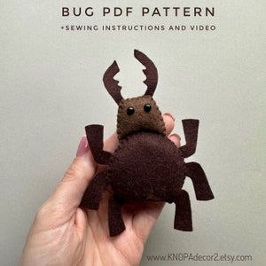 Könnte beinhalten: Ein handgefertigtes Käfer aus Filz in Brauntönen. Der Käfer hat große Zangen, sechs Beine und zwei kleine, runde Augen. Der Text "BUG PDF PATTERN + SEWING INSTRUCTIONS AND VIDEO" befindet sich oben im Bild.