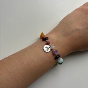 Puede incluir: Un brazalete con un dije de arcoíris de plata que presenta un diseño de arcoíris. El brazalete está hecho con piedras de varios colores, incluyendo amarillo, naranja, rojo, rosa, morado, azul y verde.