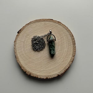 May include: A silver chain necklace with a green and black crystal pendant. The pendant is shaped like a point and has a silver cap on top.
