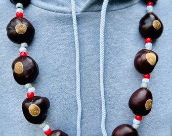 May include: A necklace made of brown buckeyes with red and white beads. The necklace is worn on a gray hoodie.