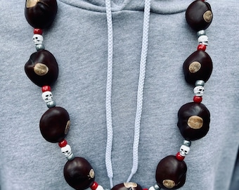 May include: A necklace made of brown, round, natural objects with white skull beads and red beads. The necklace is worn on a gray hoodie.