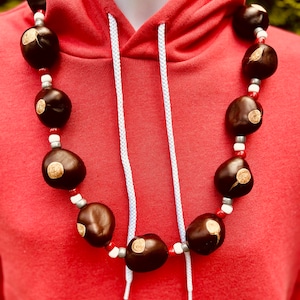May include: A red hoodie with a white drawstring and a necklace made of brown nuts with white and red beads.