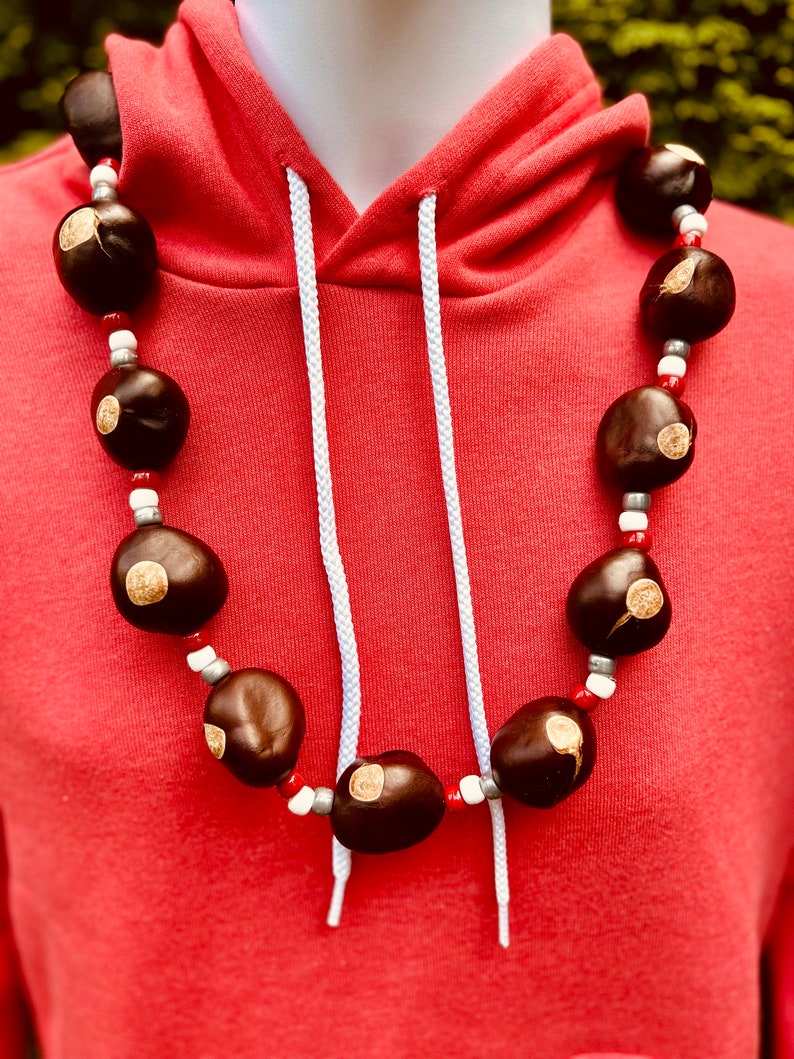 May include: A red hoodie with a white drawstring and a necklace made of brown nuts with white and red beads.