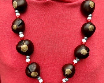 May include: A red hoodie with a necklace made of brown chestnuts and white and red beads. The necklace has a gold pendant with the number "614" on it.