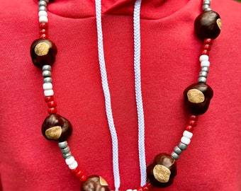 May include: A red hoodie with a white drawstring and a necklace made of brown chestnuts, red, white, and silver beads.