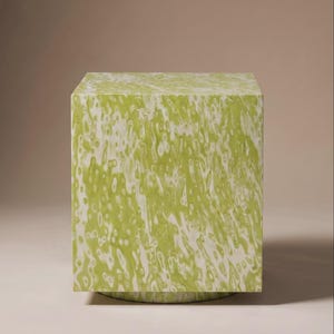 May include: A square, lime green side table with a white, marbled pattern. The table is cube-shaped and rests on a circular base. The design has a modern aesthetic.