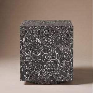 May include: A square, decorative block with a unique pattern. The block is primarily dark gray with a white, swirling design across all sides. The design resembles a topographical map or flowing water. The block is a solid color and has a smooth finish.