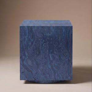 May include: A blue cube-shaped side table with a swirling, wood-grain pattern. The table sits on a circular base, creating a modern, geometric design. The colour is a deep, muted blue, suitable for various interior styles.