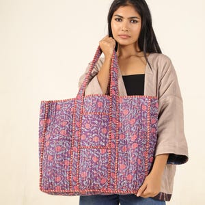 May include: A large purple and pink floral tote bag with a smaller pocket on the front. The bag is made of quilted fabric and has a  stitched design.