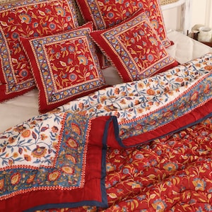 May include: A red and white floral patterned quilt with a navy blue border. The quilt is folded and has several matching throw pillows with the same floral pattern.